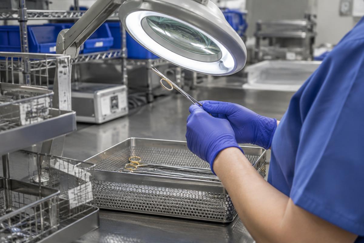 Sterile processing technician inspecting a surgical instrument under a magnifier